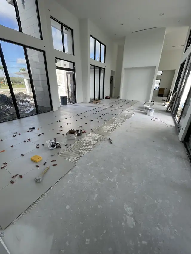 Large porcelain floor tiles being laid with leveling clips in a bright open room with tall windows