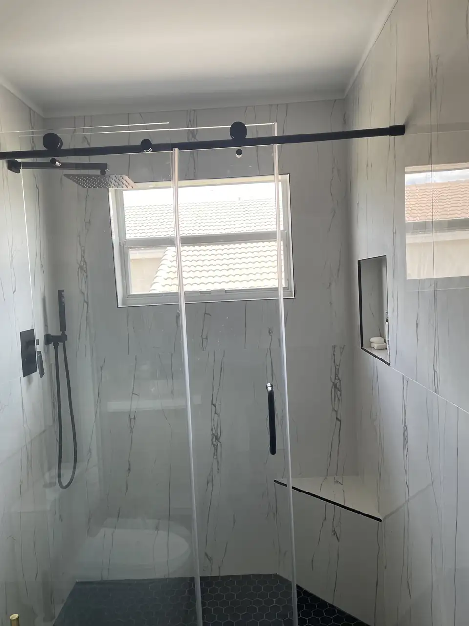Walk-in shower with glass door, marble-look porcelain walls, matte black fixtures and a built-in niche, bathroom remodeling Palm Beach County