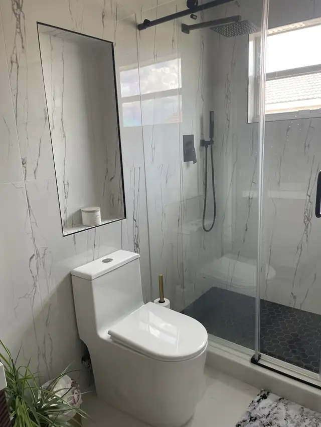 Remodeled bathroom with glass shower, marble-look porcelain walls, dark mosaic shower floor and new toilet