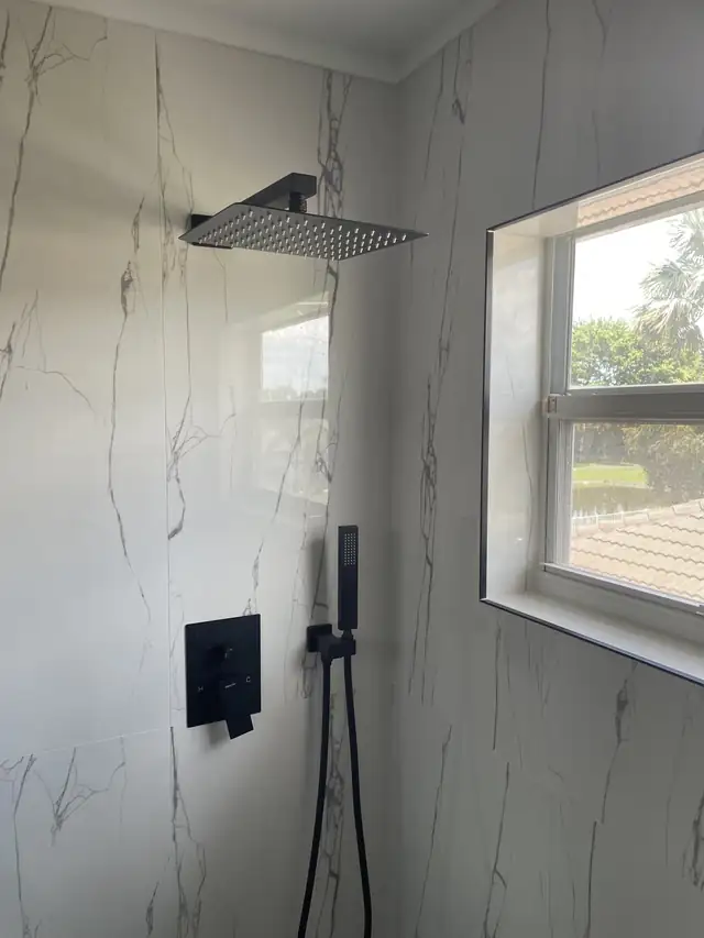 Walk-in shower with rain shower head, black handheld sprayer and tiled window sill in marble-look porcelain