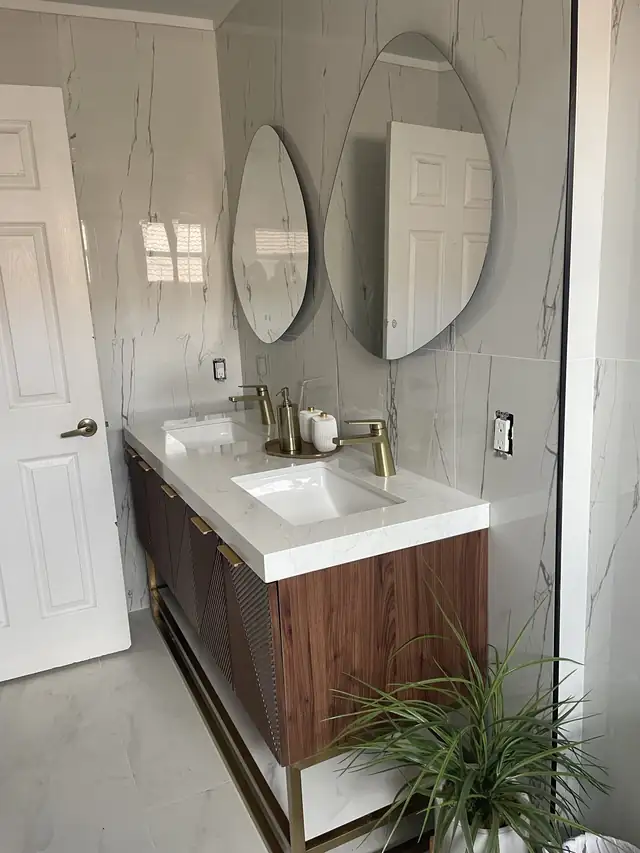 Walnut vanity with a white top, brass faucets and two round mirrors against marble-look porcelain walls